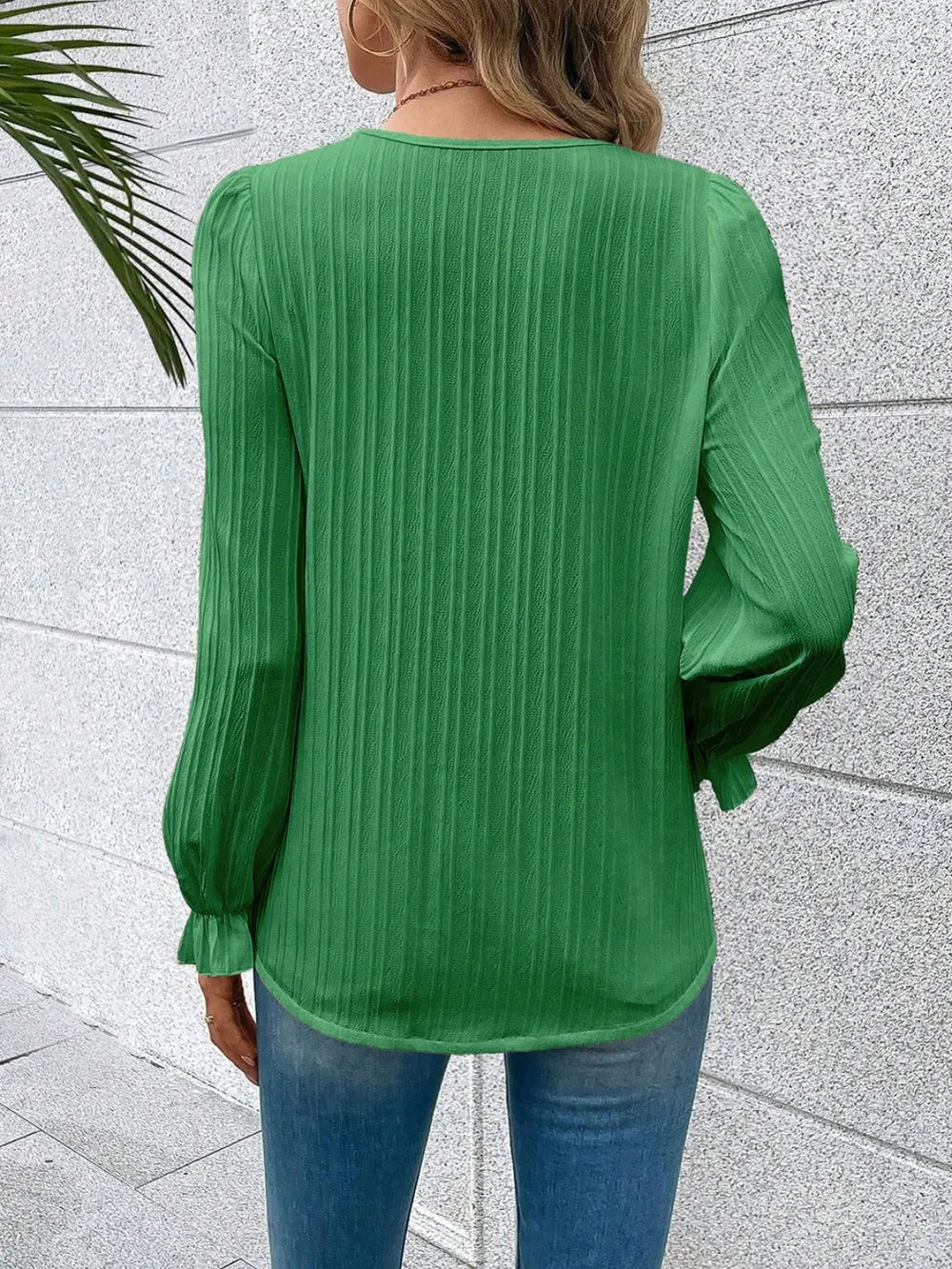 Green ribbed blouse worn by a person against a light gray wall.