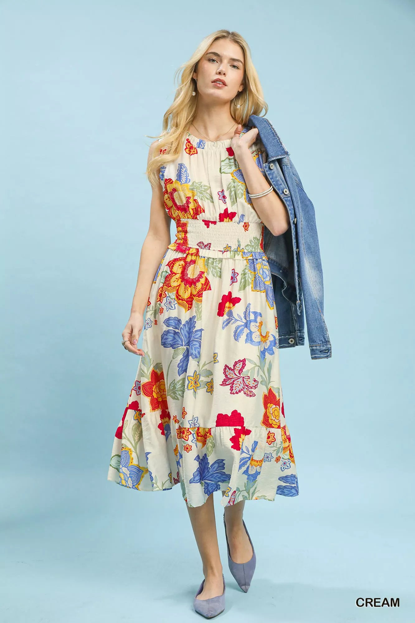 Woman wearing a colorful floral dress with a denim jacket on a light blue background