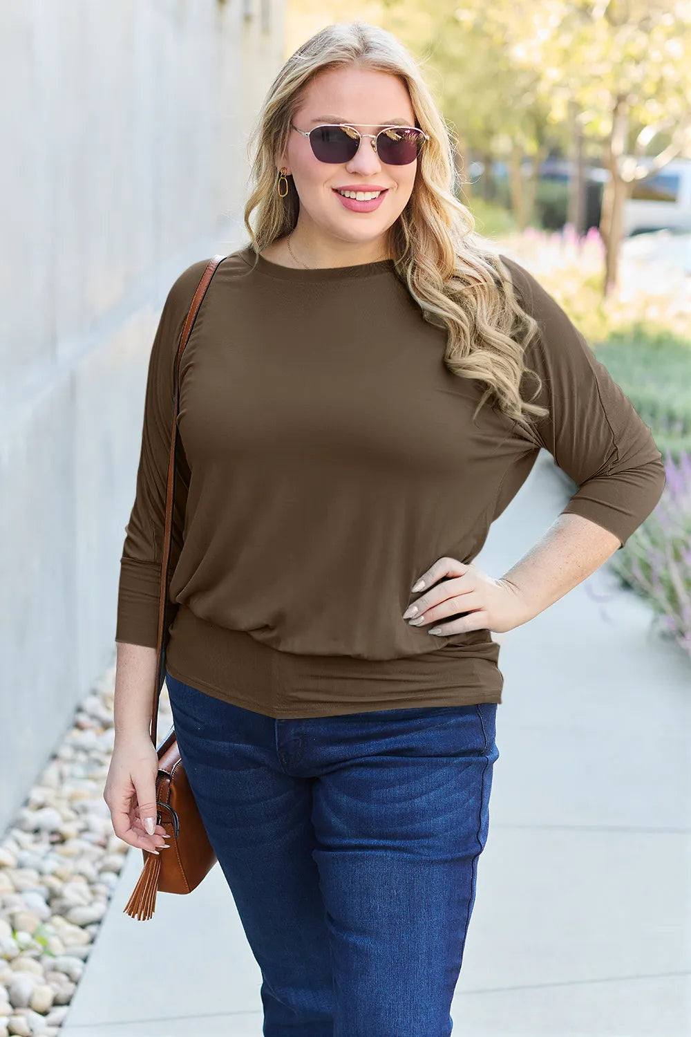 Woman wearing a brown top and blue jeans standing outdoors.