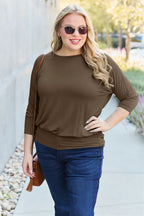 Woman wearing a brown top and blue jeans standing outdoors.