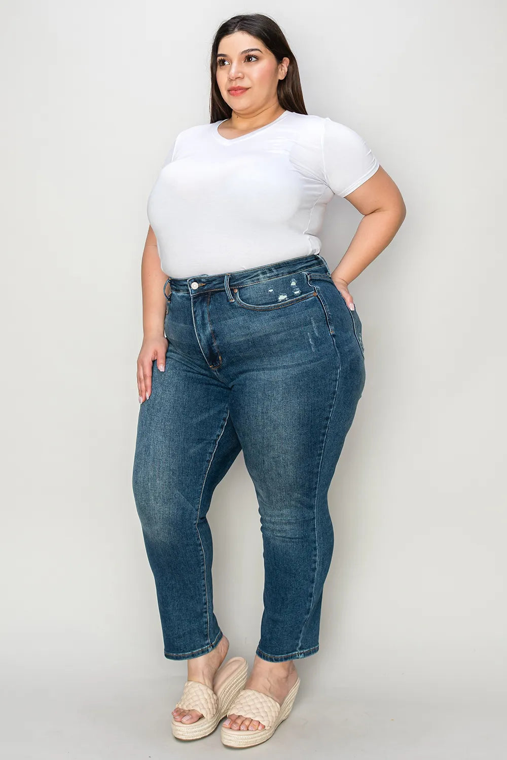 Woman wearing blue jeans and a white t-shirt against a plain background
