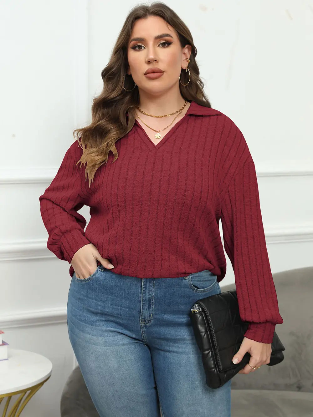 Woman wearing a burgundy sweater and blue jeans holding a black clutch.