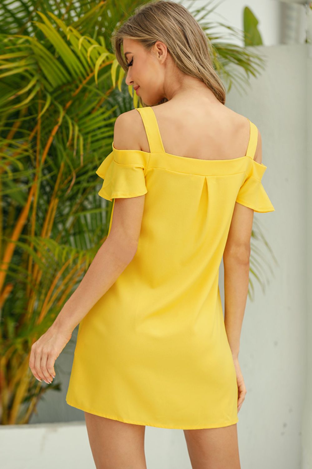 Woman wearing a yellow off-shoulder dress with green foliage in the background
