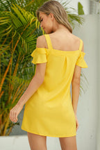 Woman wearing a yellow off-shoulder dress with green foliage in the background