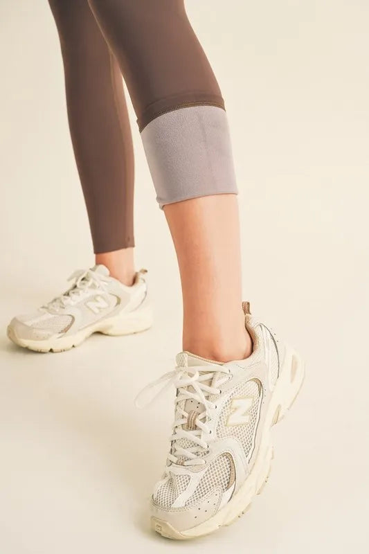 Person wearing beige athletic shoes and dark leggings on a neutral background
