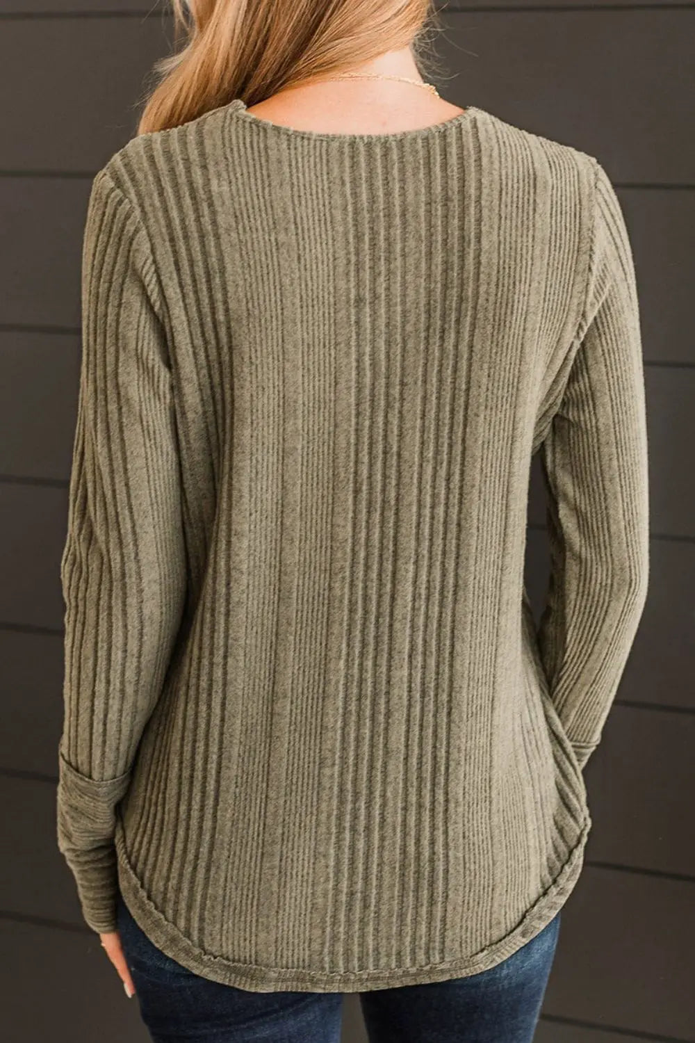 Person wearing a ribbed green sweater against a dark background