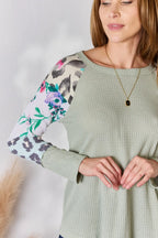 Woman wearing a green sweater with floral and animal print sleeves on a plain background