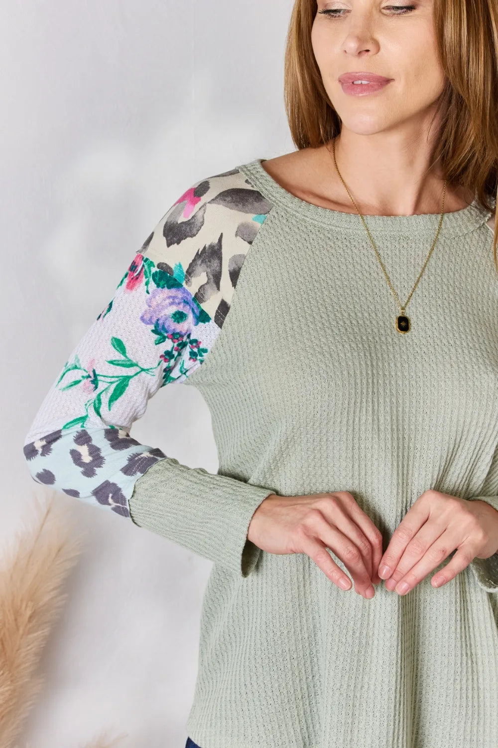 Woman wearing a green sweater with floral and animal print sleeves on a plain background