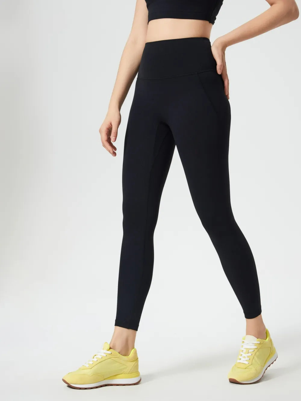 Person wearing black leggings and yellow sneakers on a white background