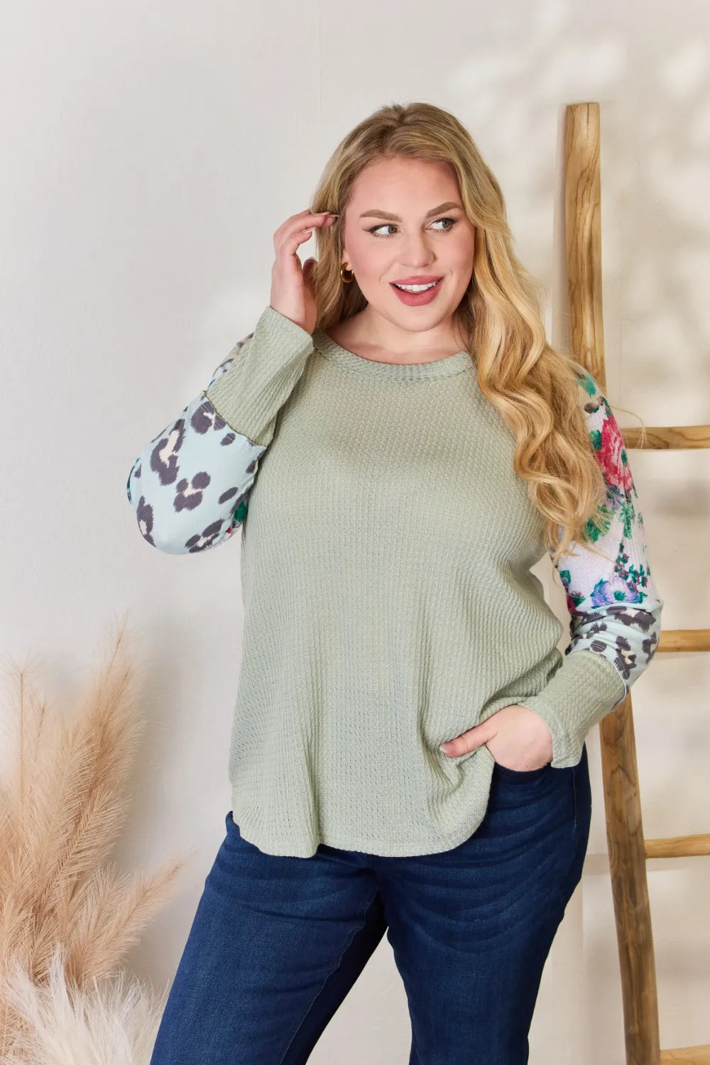 Woman wearing a green sweater with floral sleeves against a neutral background