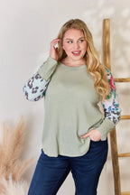 Woman wearing a green sweater with floral sleeves against a neutral background