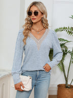 Woman wearing a light blue sweater and jeans, holding a white clutch, with a plant in the background.