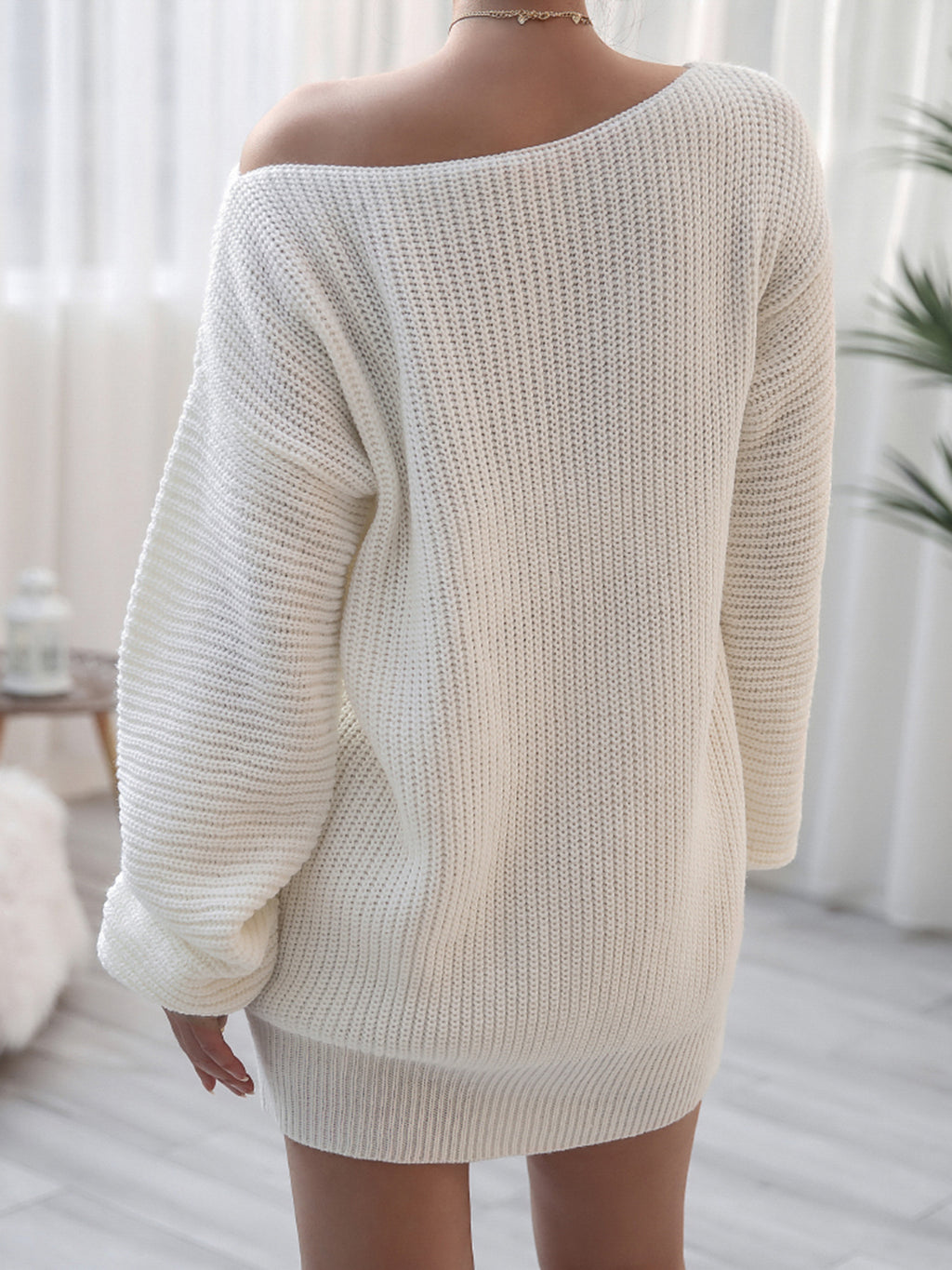 Person wearing a white oversized sweater in a bright room with curtains.