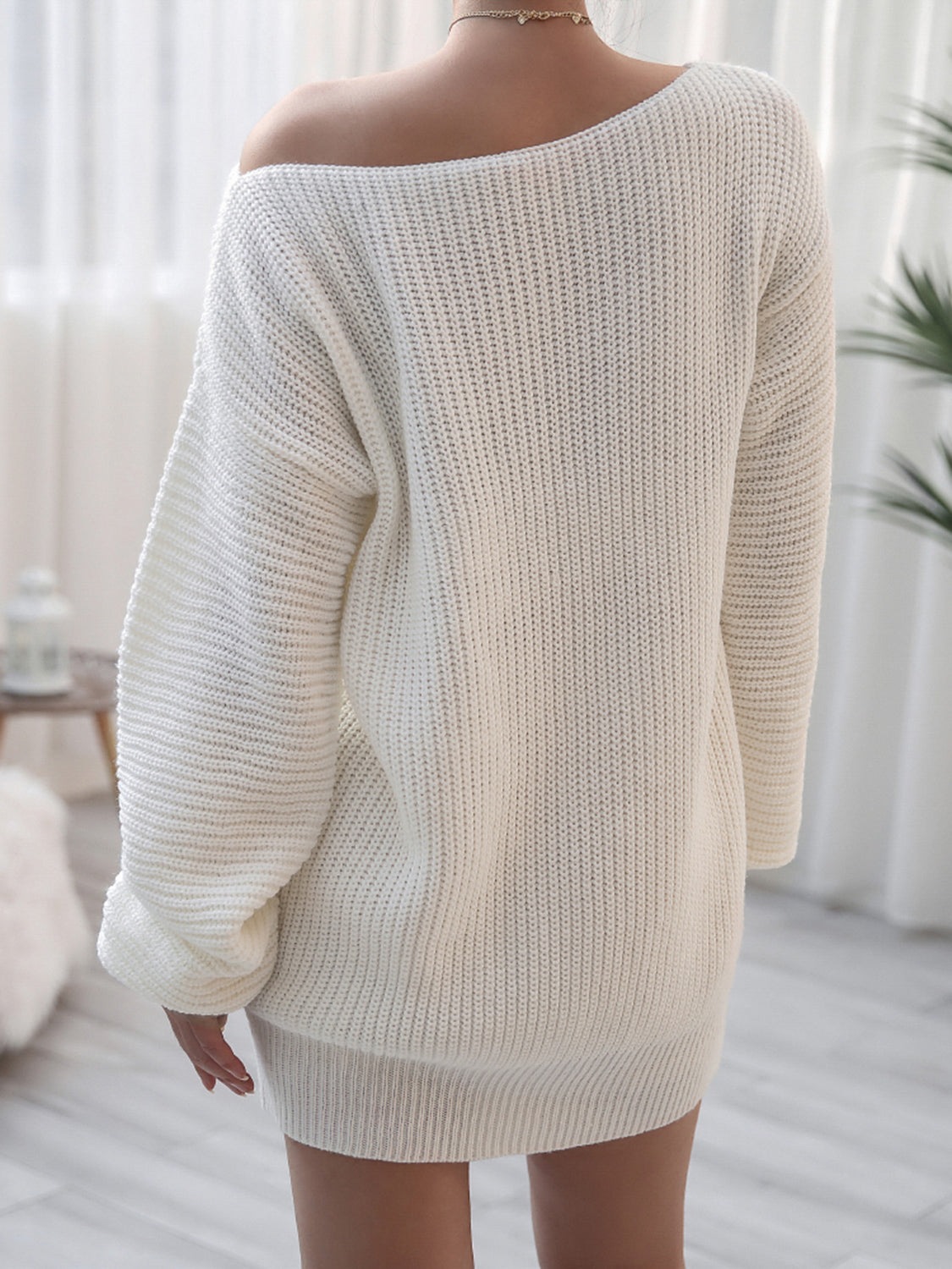 Person wearing a white oversized sweater in a bright room with curtains.