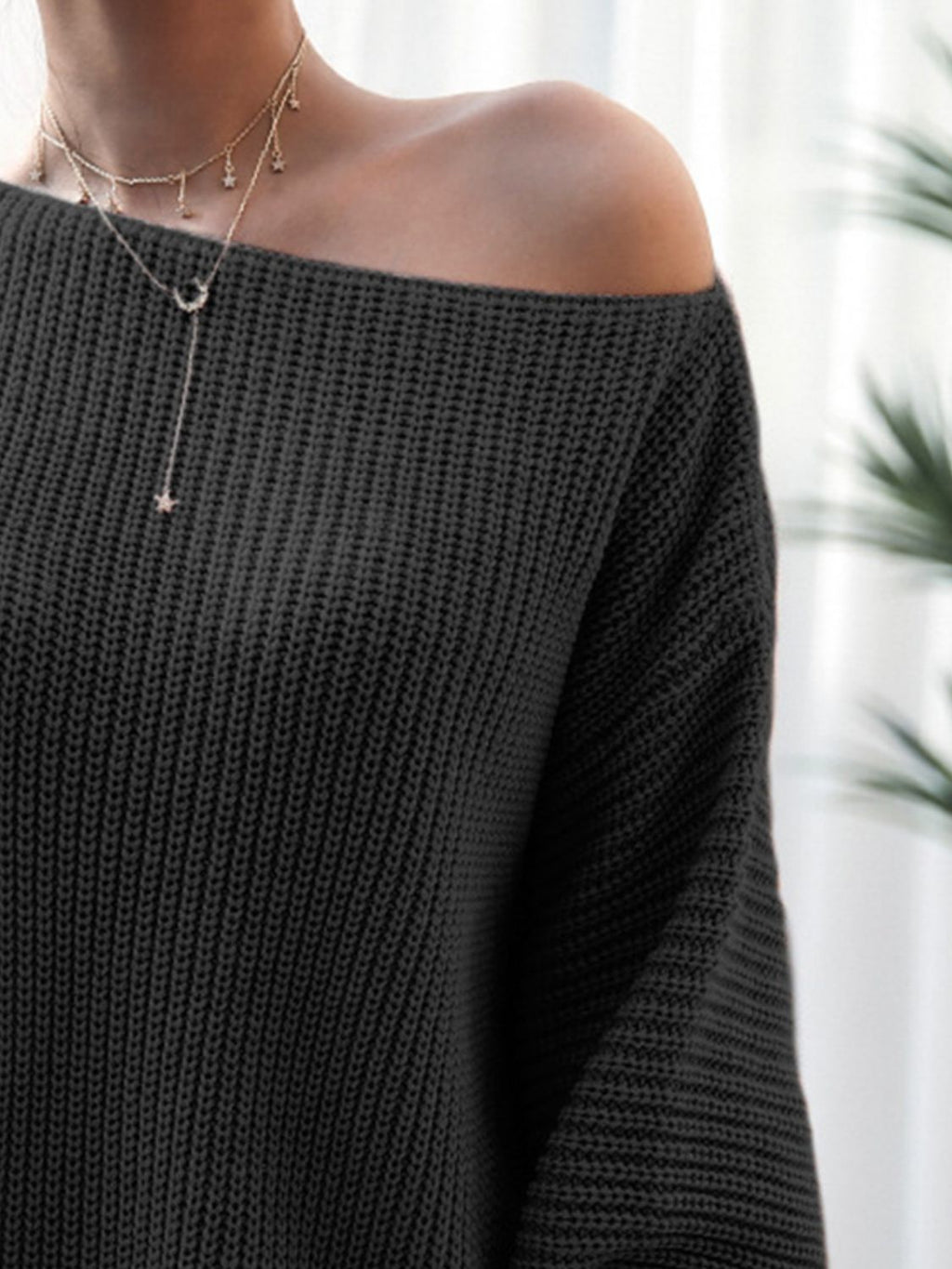 Black off-shoulder sweater worn by a person with a blurred background