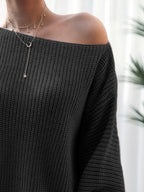 Black off-shoulder sweater worn by a person with a blurred background