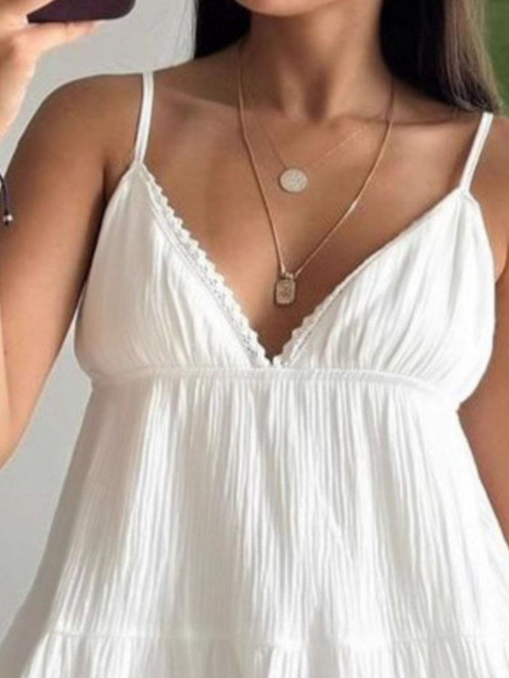 Woman wearing a white dress with thin straps and a gold necklace.
