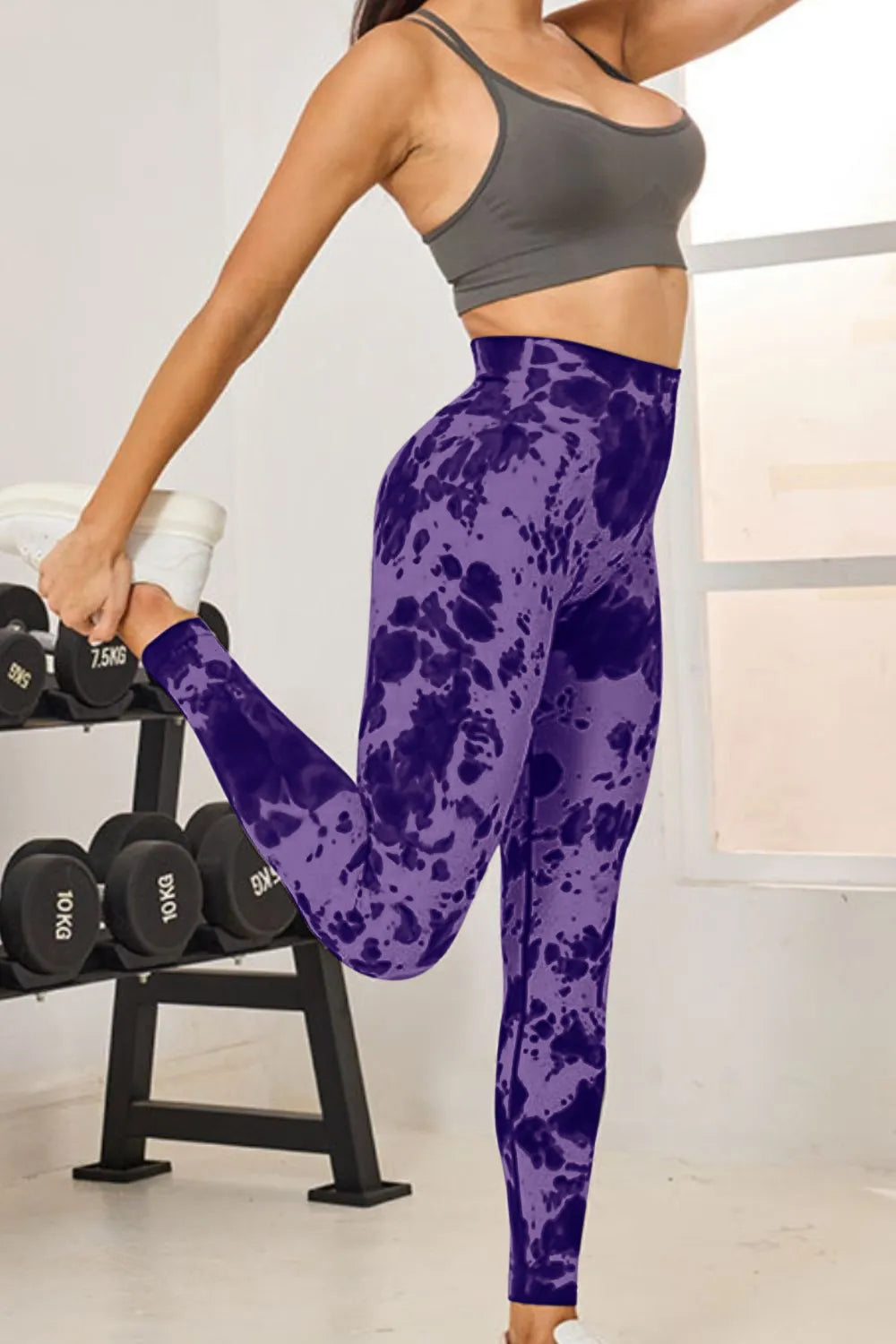 Person wearing purple tie-dye leggings and gray sports bra in a gym setting
