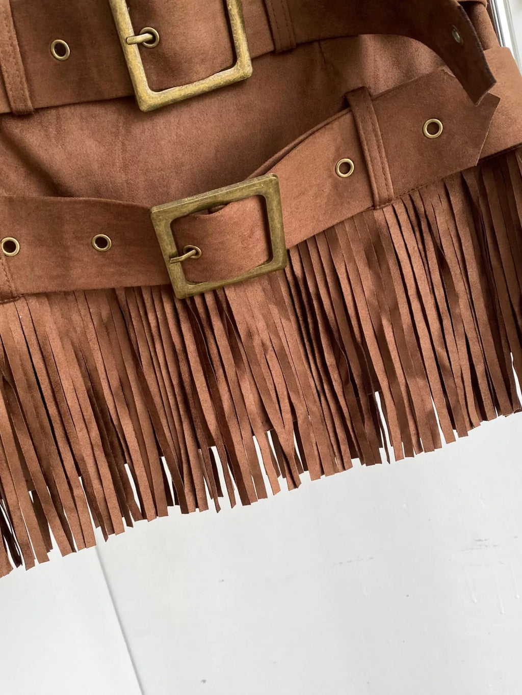Brown suede jacket with fringe details and gold buckles on a white background