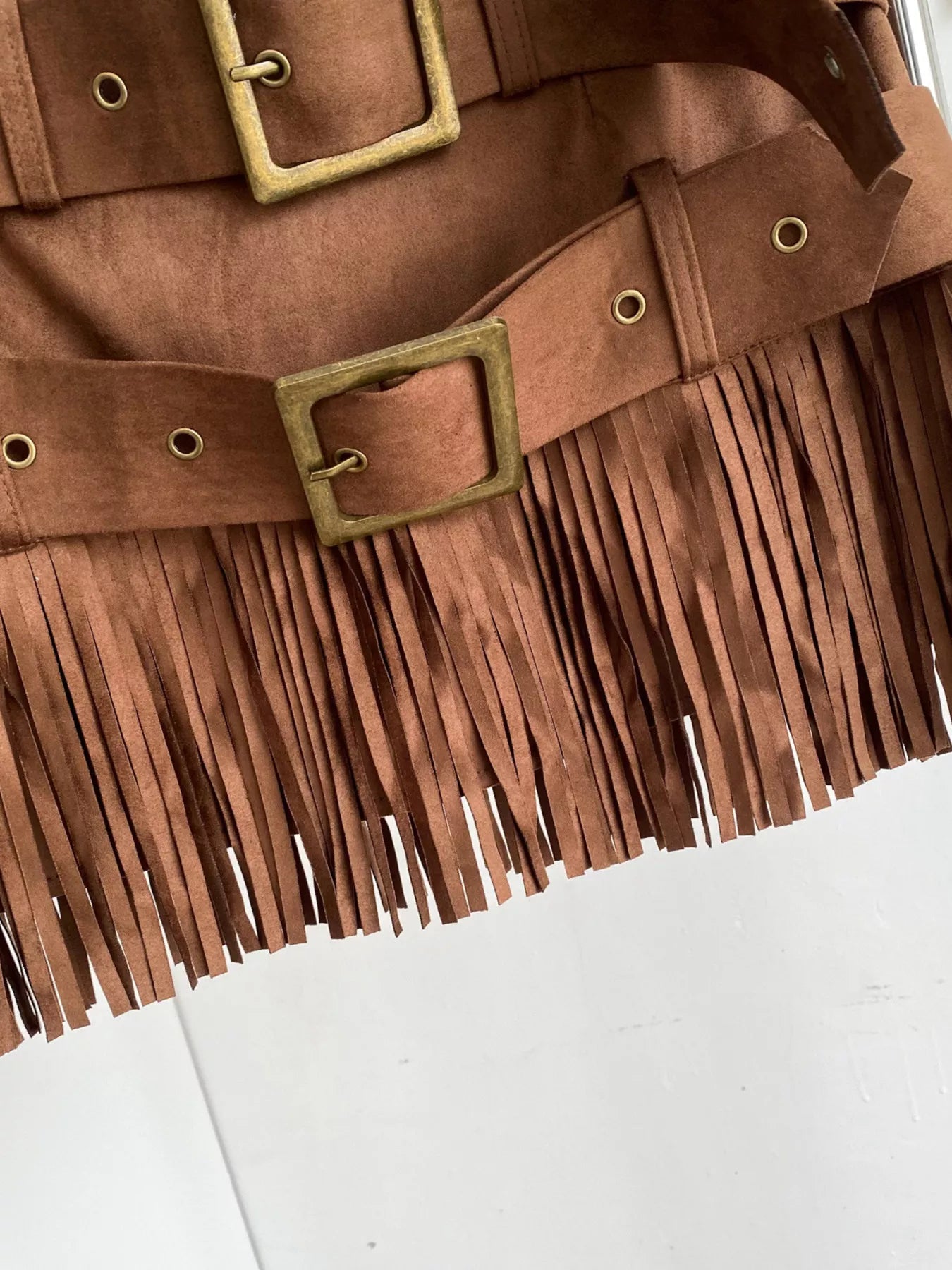 Brown suede jacket with fringe details and gold buckles on a white background