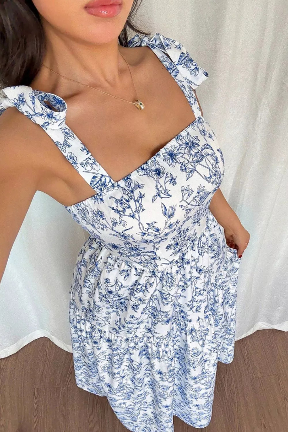 Woman wearing a blue floral dress with a white curtain background