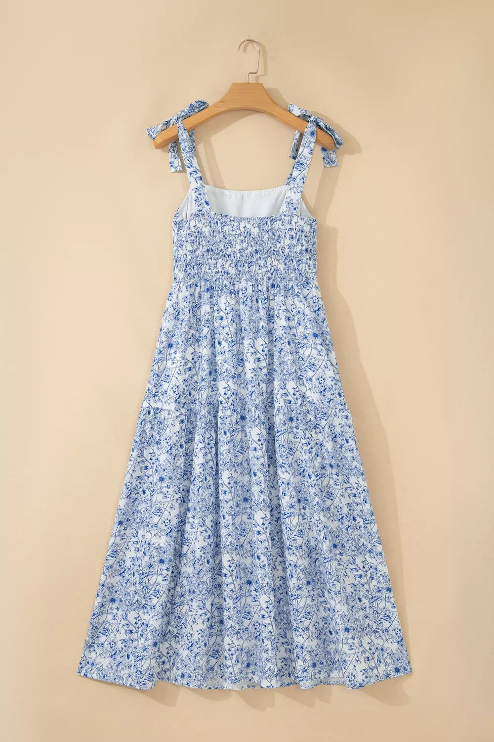 Blue floral dress on a wooden hanger against a beige background