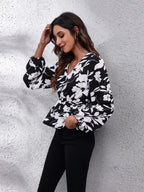Woman wearing a black and white floral blouse against a textured white wall.