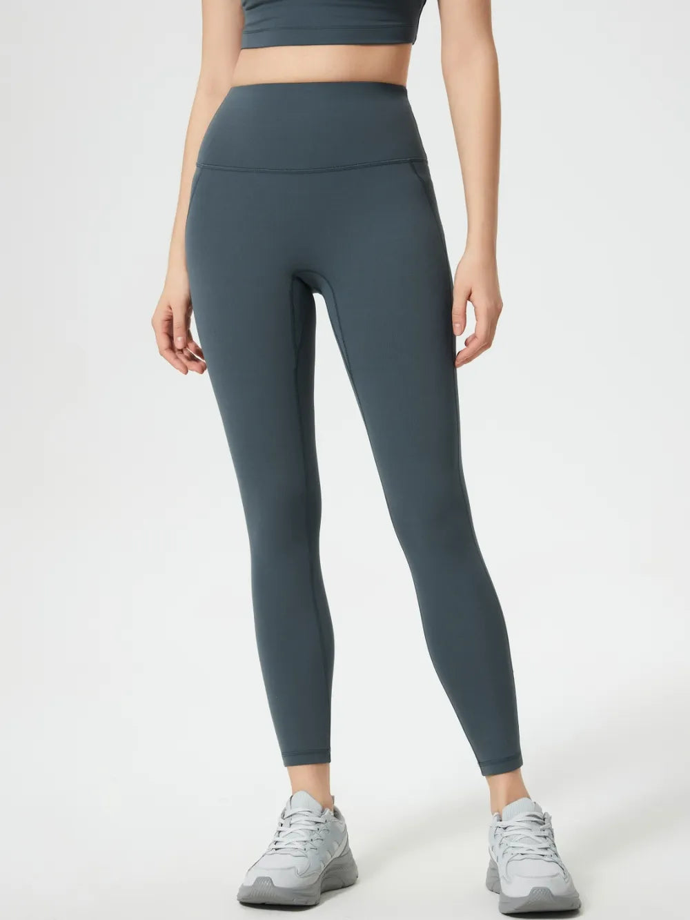 Person wearing dark gray leggings and a black sports bra on a white background