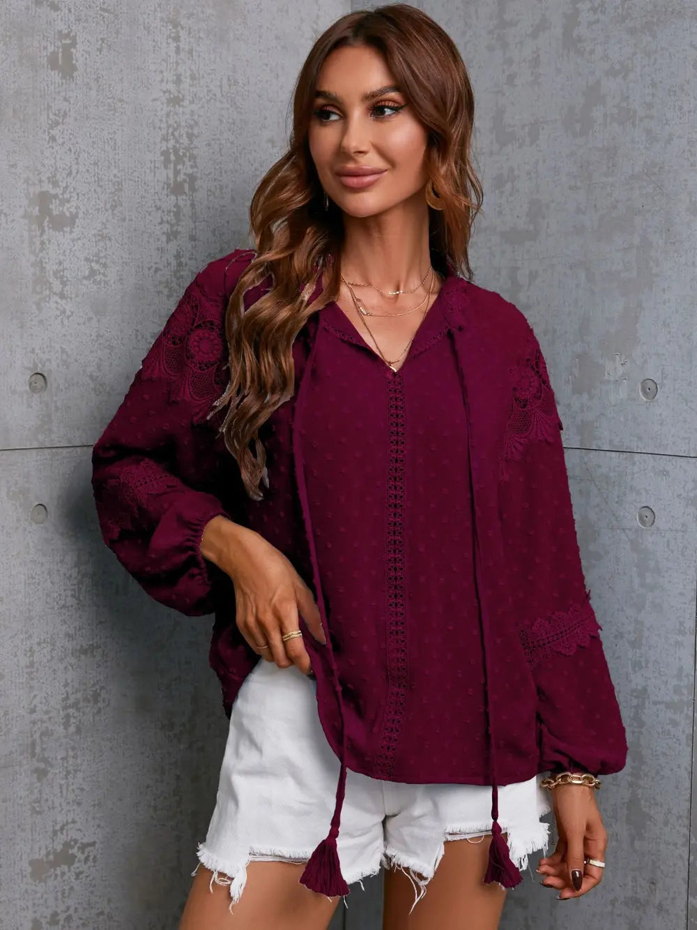 Woman wearing a burgundy blouse with tassels against a gray concrete wall
