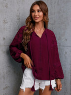 Woman wearing a burgundy blouse with tassels against a gray concrete wall