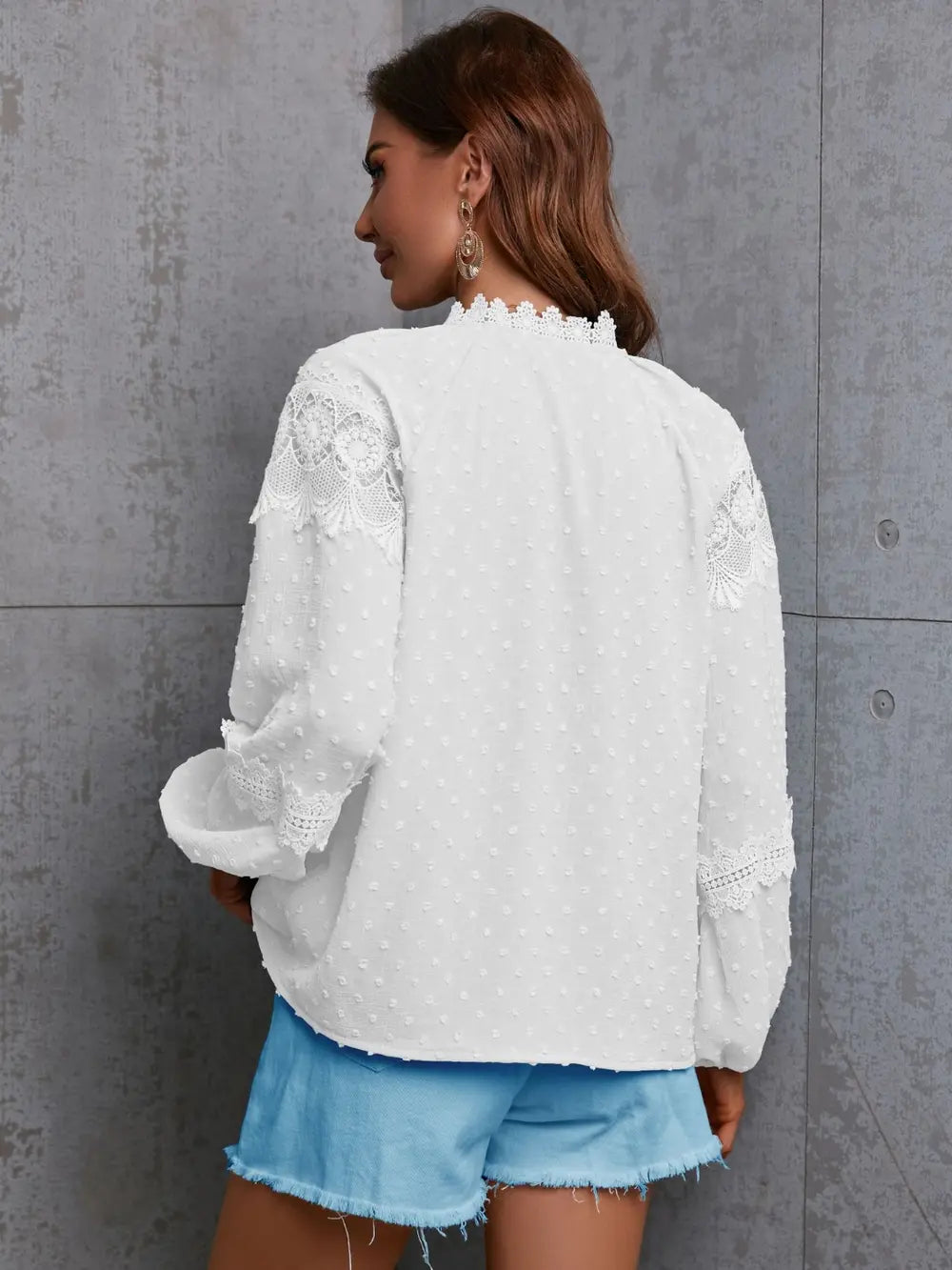 Woman wearing a white lace top and blue shorts against a gray wall