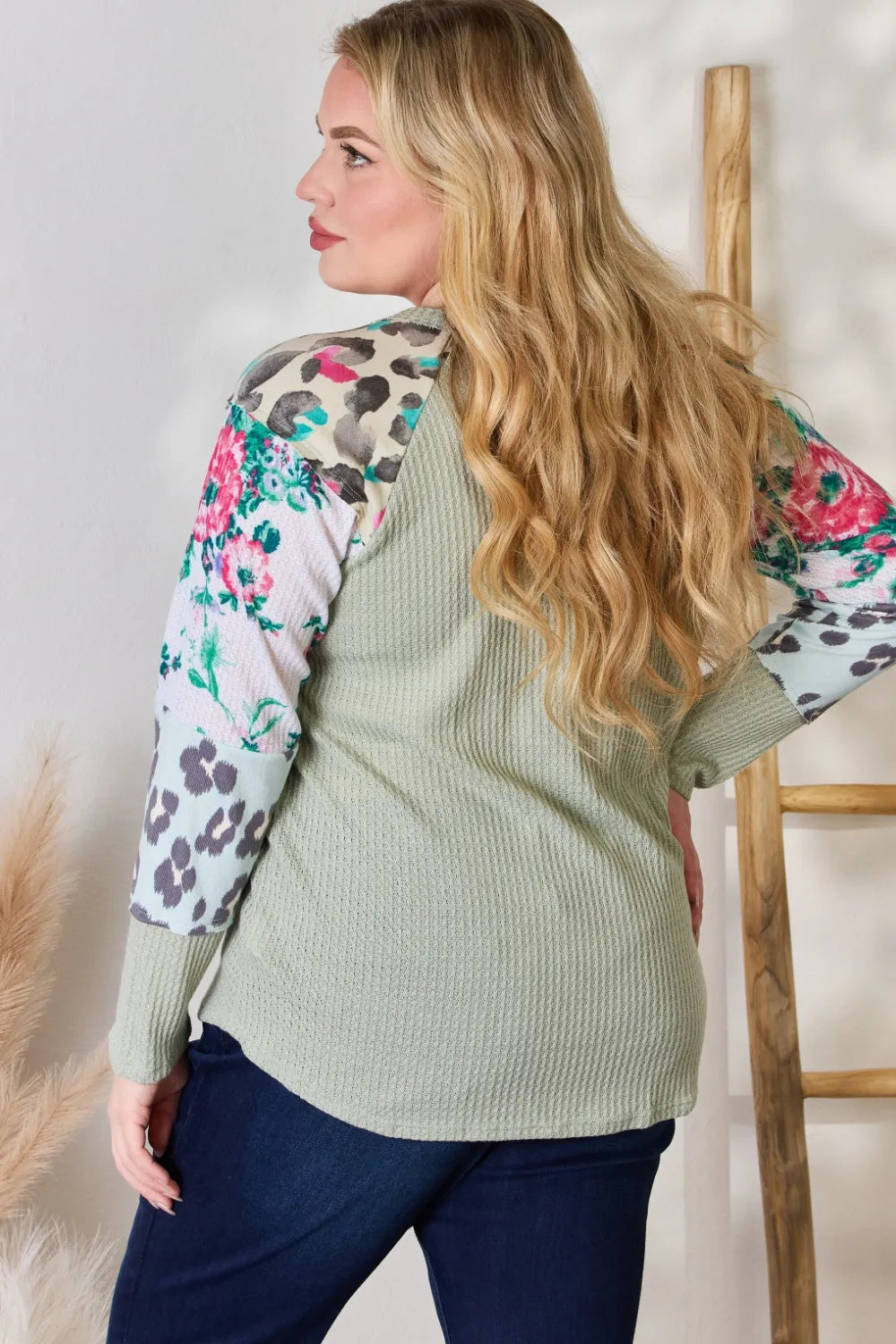 Woman wearing a green ribbed sweater with floral and leopard print sleeves against a neutral background.