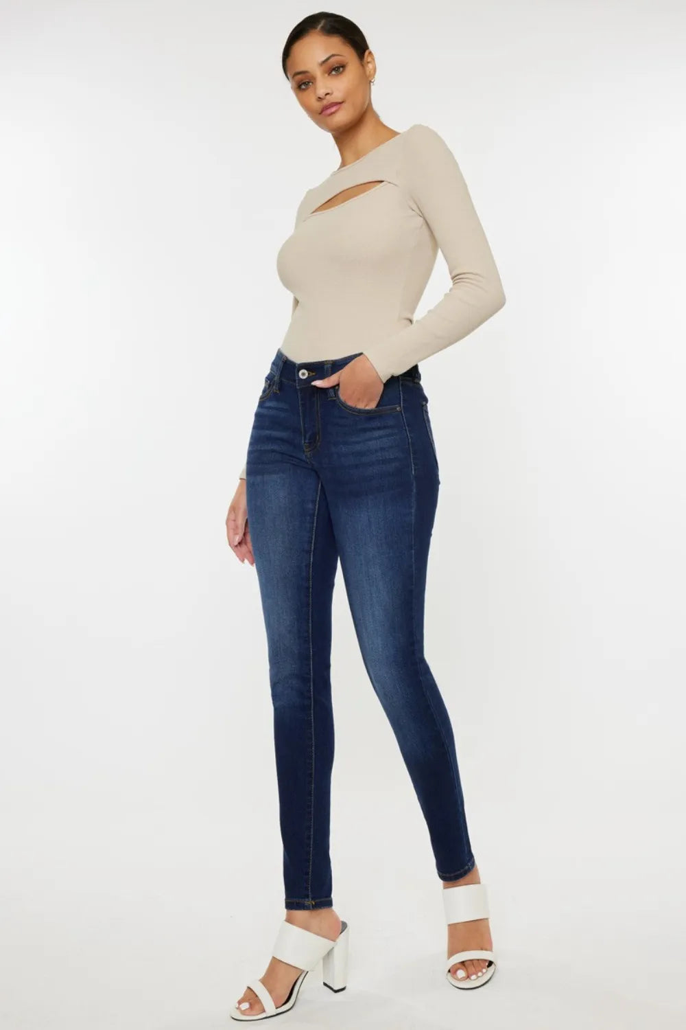 Woman wearing a beige long-sleeve top and blue jeans on a white background