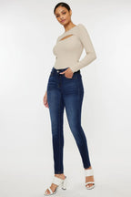 Woman wearing a beige long-sleeve top and blue jeans on a white background