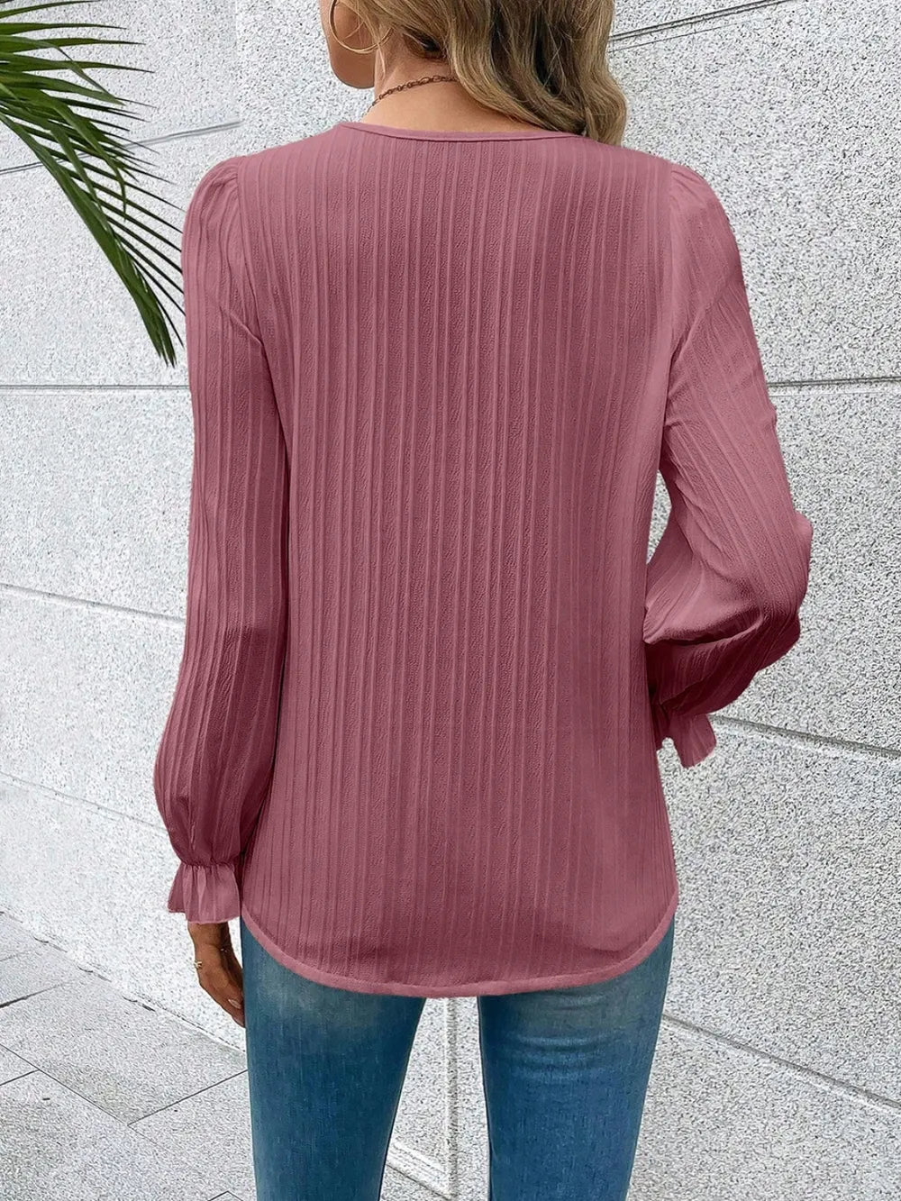 Person wearing a pink ribbed blouse with long sleeves against a light gray wall.