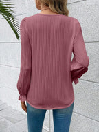 Person wearing a pink ribbed blouse with long sleeves against a light gray wall.
