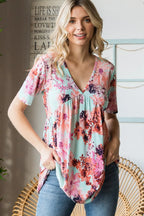 Woman wearing a floral blouse standing indoors with a decorative wall in the background
