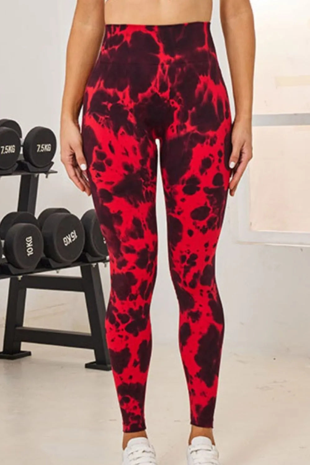 Person wearing red and black patterned leggings in a gym setting with weights in the background.