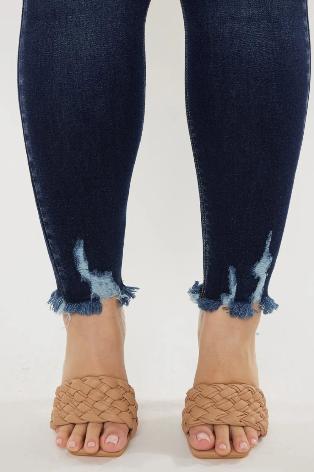 Navy blue distressed jeans worn with tan woven sandals on a white background