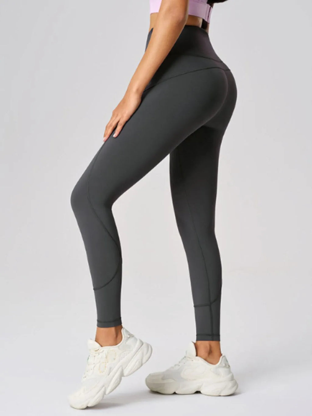 Person wearing dark gray leggings and white sneakers on a light gray background