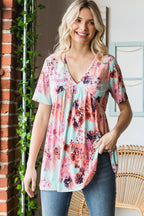 Woman wearing a floral blouse standing in a room with a brick wall and wicker chair.