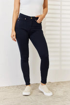 Person wearing black jeans and white sneakers against a white wall.