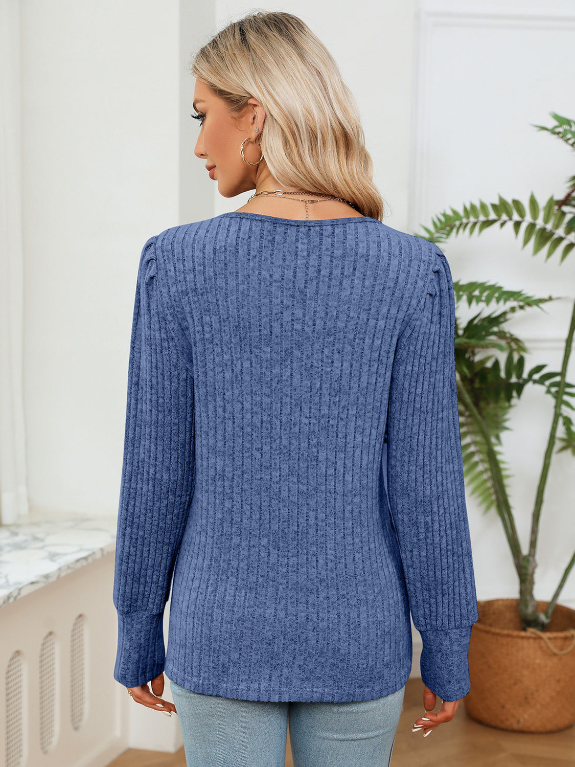 Woman wearing a blue sweater in a room with a plant