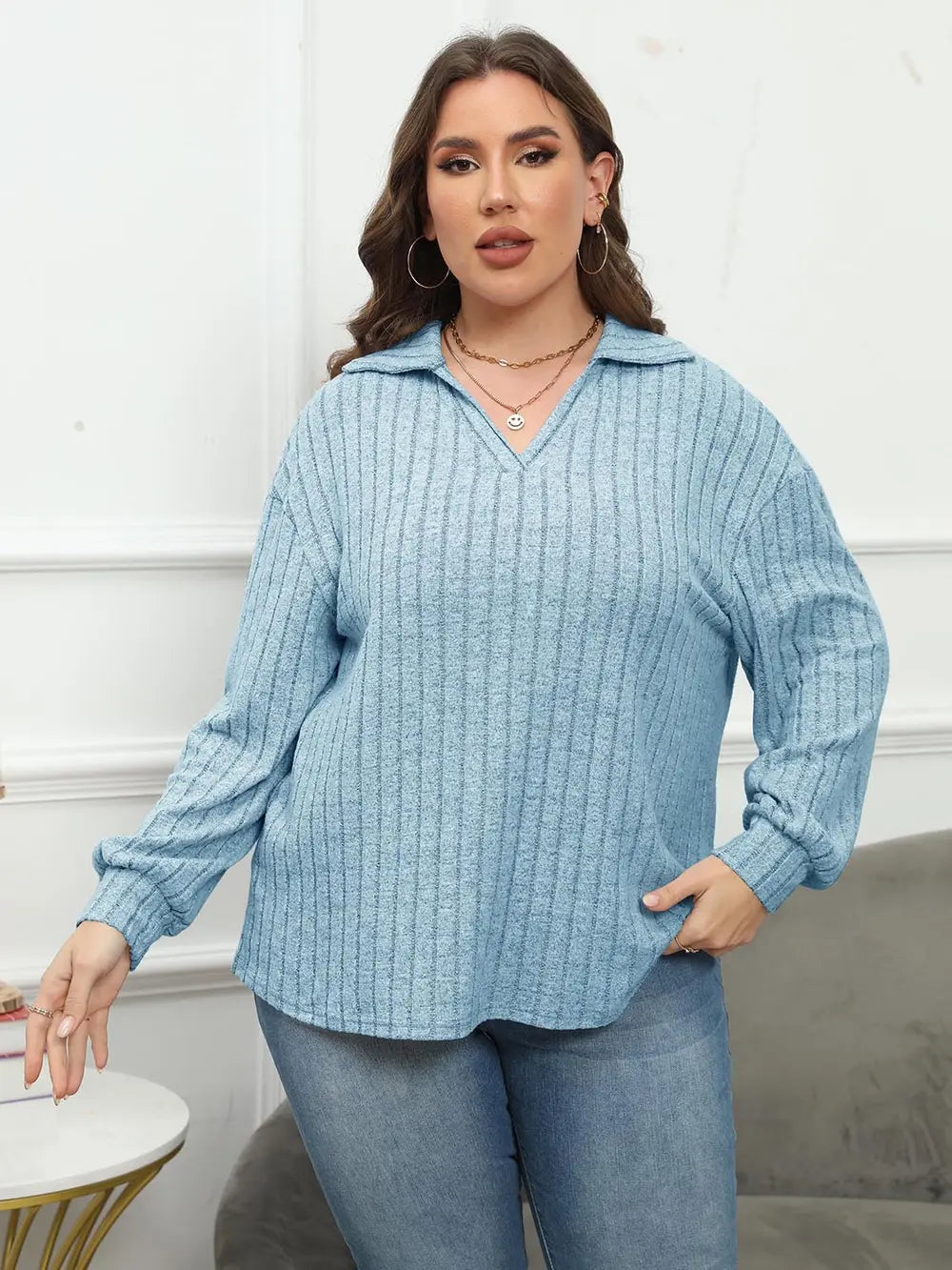 Woman wearing a blue ribbed sweater and jeans in a neutral setting