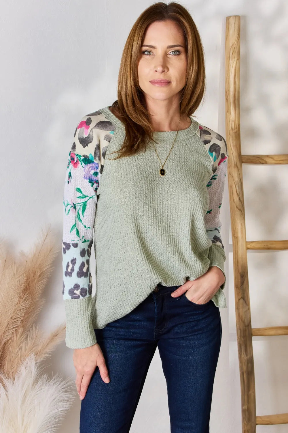 Woman wearing a light green sweater with floral and animal print sleeves against a white background.