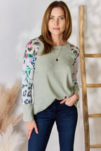 Woman wearing a light green sweater with floral and animal print sleeves against a white background.