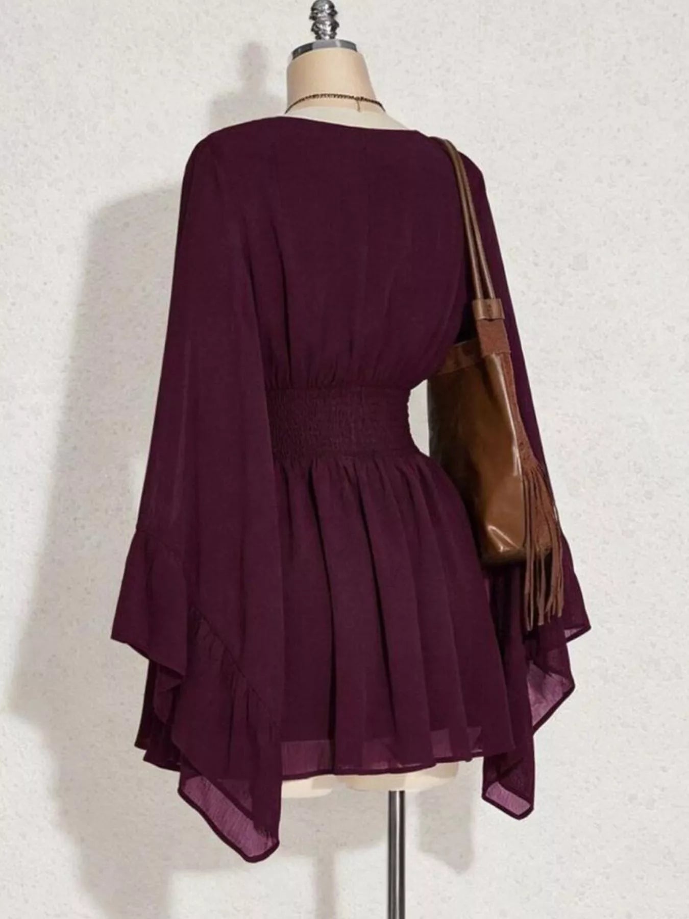 Purple dress on a mannequin with a brown handbag against a white background
