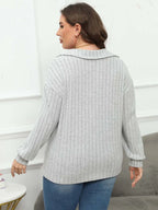 Woman wearing a light gray ribbed sweater and blue jeans in a minimal indoor setting.