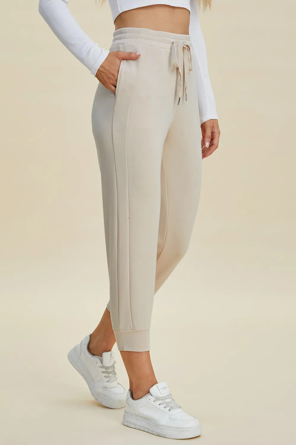 Person wearing beige jogger pants and white sneakers on a beige background