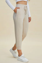 Person wearing beige jogger pants and white sneakers on a beige background